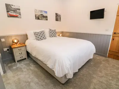 a bedroom with a white bed and a tv on the wall at Nana's Cottage in Camborne
