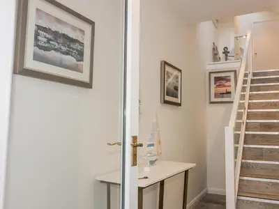 a hallway with a staircase and a door with a table at Midships in St Austell