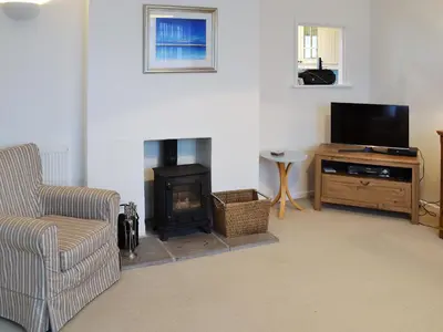 a living room with a fireplace and a chair and a television at Chynoweth in Saint Keverne