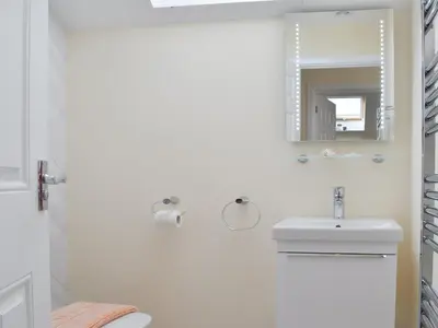 a white bathroom with a sink and a mirror at Driftwood in Port Isaac