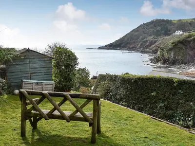 a wooden bench sitting in the grass near the ocean at Sea View - Uk30589 in Talland