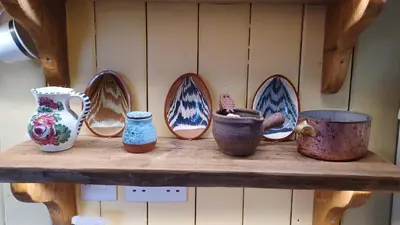 a shelf with vases and pots on a wall at Truly Paradise Cottage in Golant