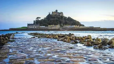a beach with rocks and a castle on a hill at Marazion Hotel in Marazion