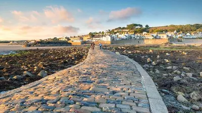 a stone path on a beach with a town in the background at Marazion Hotel in Marazion