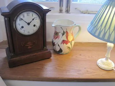 a clock and a vase on a table with a lamp at Little Pengelly Farm in Crowan