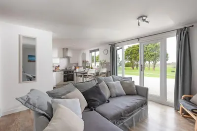 a living room with a gray couch and a kitchen at Wheal Jewel- Beautifully Fitted Wooden Lodge Helston Cornwall in Helston