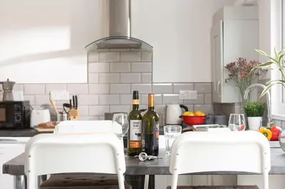 a kitchen with two white chairs and wine bottles on a table at Wheal Jewel- Beautifully Fitted Wooden Lodge Helston Cornwall in Helston