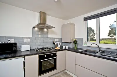 a white kitchen with a stove and a sink at Wheal Amelia- Beautifully Fitted Wooden Lodge Helston Cornwall in Helston