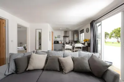 a living room with a gray couch and a kitchen at Wheal Prosper- Beautifully Fitted Wooden Lodge Helston Cornwall in Helston