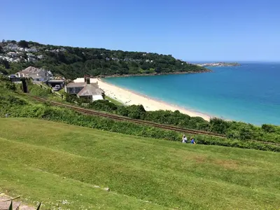 a group of people sitting on a grassy hill next to a beach at Beach View in St Ives