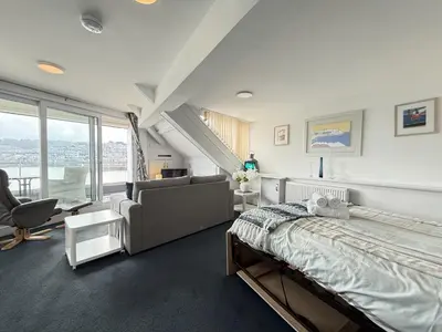 a bedroom with a bed and a chair and window at Crows Nest - panoramic views of St Ives harbour in St Ives