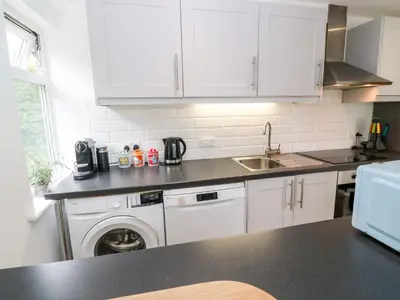 a kitchen with white cabinets and a washing machine at The Poop Deck in Helston