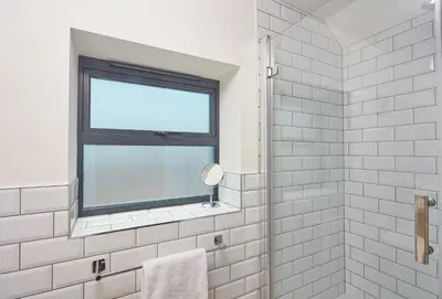 a bathroom with a window and a white tiled shower at The Larches in St. Agnes