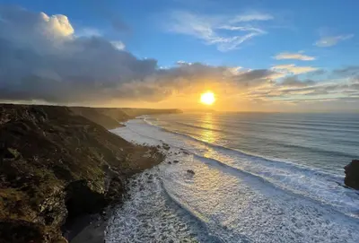 a sunset over a beach with the sun setting at The Larches in St. Agnes