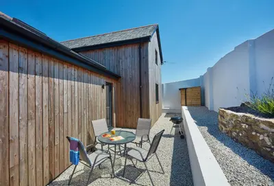 a patio with a table and chairs next to a fence at The Larches in St. Agnes