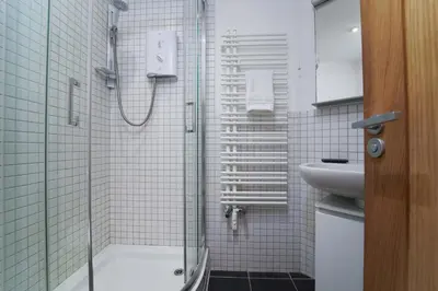 a white tiled bathroom with a shower and a sink at Island Wastrel in St Ives