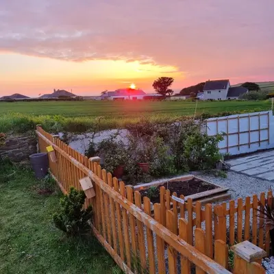 a fence in a field with the sunset in the background at Hegarty's cottage at Trevarrian Lodge in Mawgan Porth