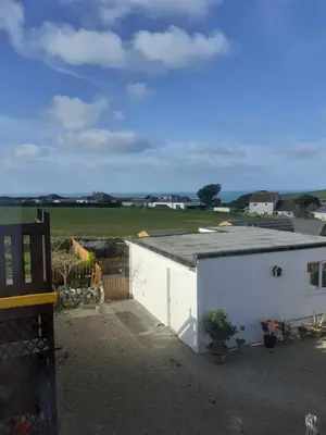 a white building with a roof with a field in the background at Hegarty's cottage at Trevarrian Lodge in Mawgan Porth