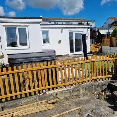 a house with a wooden fence in front of it at Hegarty's cottage at Trevarrian Lodge in Mawgan Porth