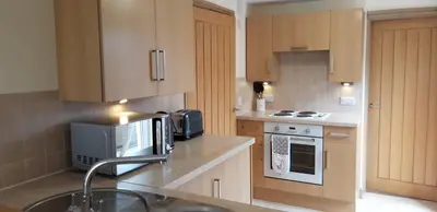 a kitchen with wooden cabinets and a sink and a microwave at Trelawne Garden Annexe in Falmouth