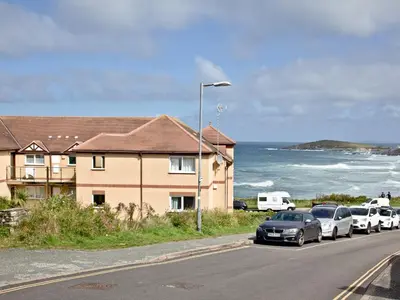 a street with cars parked next to a house and the ocean at Apartment 2 Waters Edge in Crantock