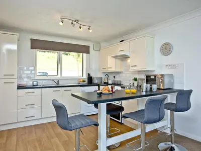 a kitchen with white cabinets and a table with chairs at Apartment 2 Waters Edge in Crantock