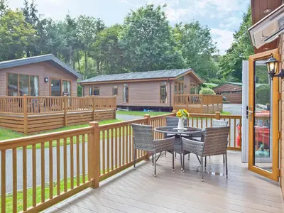 a patio with a table and chairs on a deck at Forest Glade Lodge in Lanlivery