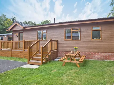 a house with a wooden deck and a picnic table at Forest Glade Lodge in Lanlivery