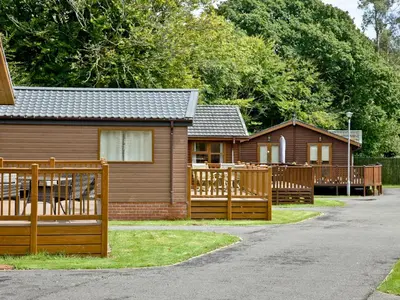 a house with a wooden fence in front of it at Forest Glade Lodge in Lanlivery