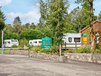 a sign in front of a campsite with two rvs at Forest Glade Lodge in Lanlivery