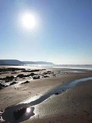 a beach with the sun shining on the sand at Chalet 26 Widemouth Bay in Bude