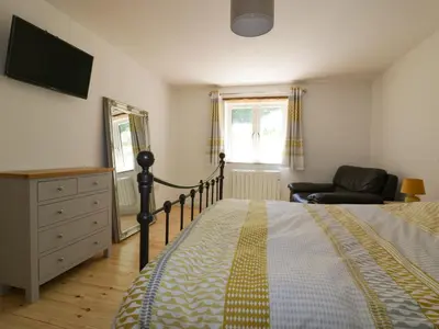 a bedroom with a bed and a television and a chair at The Cart House in St Austell