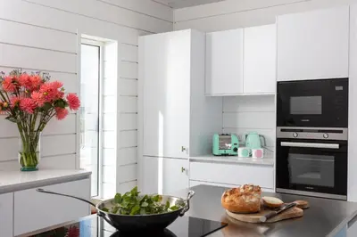 a white kitchen with a vase of flowers on a table at Three Mile Beach in Hayle