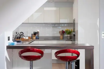 a kitchen with two red chairs at a counter at Fistral Beach Penthouse, Newquay in Crantock