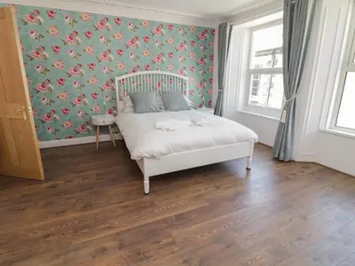 a bedroom with a white bed with a floral wallpaper at Pirate's Pad in St Austell
