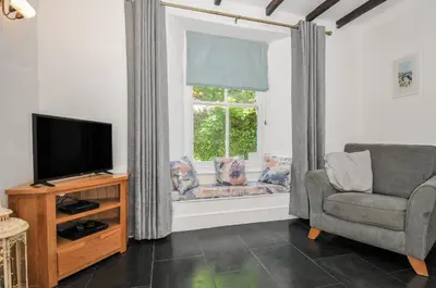 a living room with a tv and a chair and a window at Fairfield Cottage in Boscastle