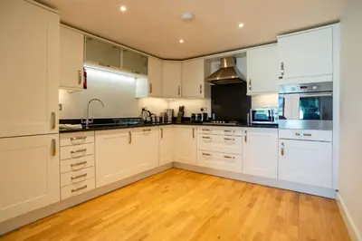 a kitchen with white cabinets and a wooden floor at Fistral Beach Garden Apartment 3 in Newquay