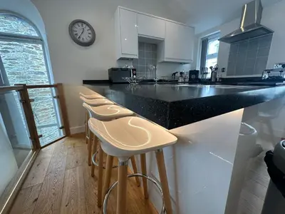 a kitchen with a counter with stools and a clock on the wall at The Old Bakery in Fowey