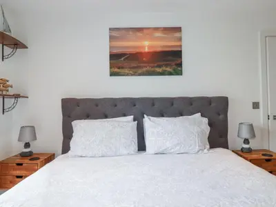 a bedroom with a white bed with two lamps and a picture at Crantock Reach in Newquay