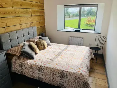 a bedroom with a bed with a wooden wall and a window at The Corn Store in St Austell