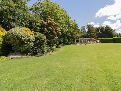 a large lawn with trees and a house in the background at Brambleside Lodge in Truro