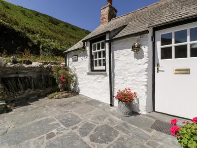 a white shed with a white door and some flowers at Harbour Cottage in Boscastle