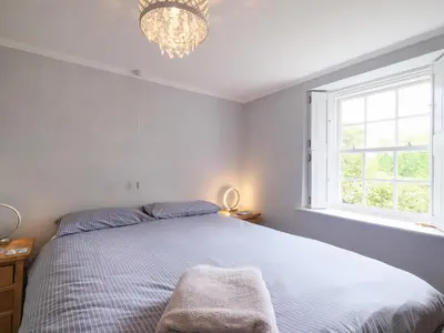 a bedroom with a bed with a chandelier and a window at Lantern Cottage in St Austell
