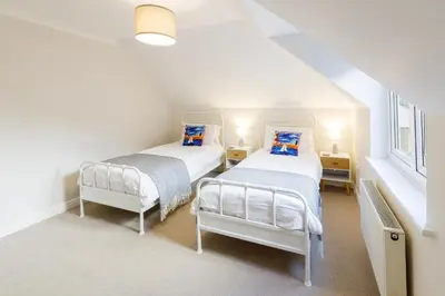 two beds in a room with white walls and windows at Breakers in Newquay