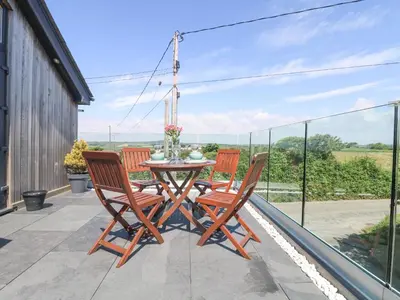 a patio with a table and chairs on a balcony at Pen Chy in Helston