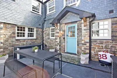 a patio with a table and benches and a blue door at Juliot 5 Star Gold Award Luxury Cottage in St Ives