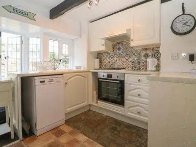 a kitchen with white cabinets and a clock on the wall at Pixie Cottage in Looe