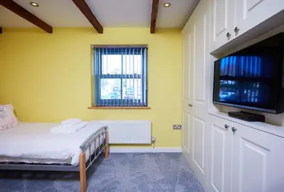 a yellow room with a bed and a flat screen tv at The Old Smoke House in St Austell