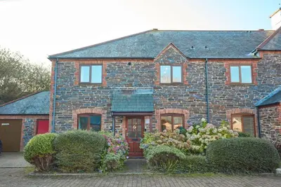 a brick house with a red door and some bushes at Trevells in Wadebridge