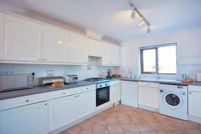 a kitchen with white cabinets and a washer and dryer at Trevells in Wadebridge